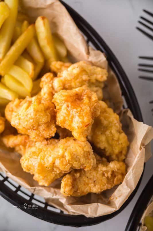 Close up of Hot Honey Popcorn Chicken and french fries in a parchment lined basket.
