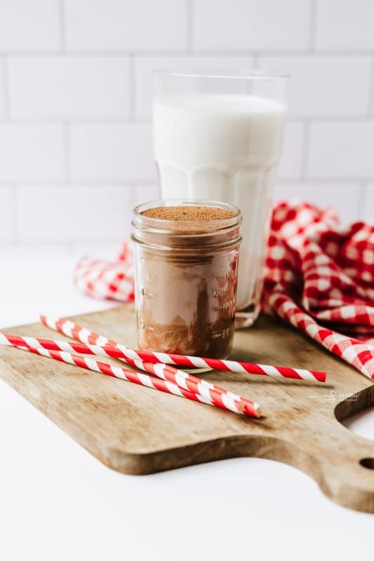 A Mason jar of Homemade Nesquik with a tall glass of milk behind it.