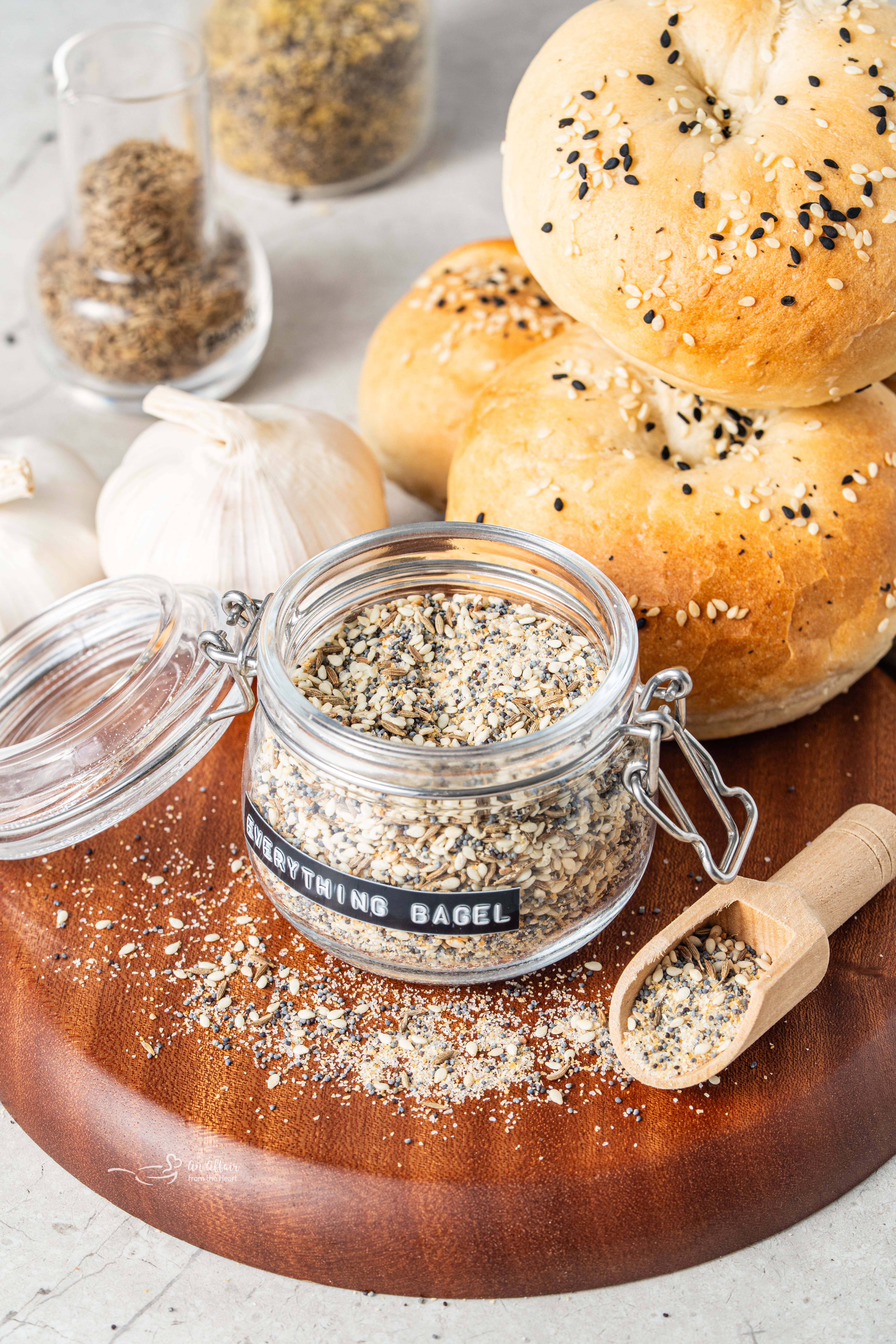 Everything Bagel Seasoning in a small glass jar next to bagels and a wooden spoon with the seasoning in it.