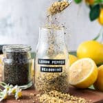 A spoon taking Lemon Pepper Seasoning out of a glass container