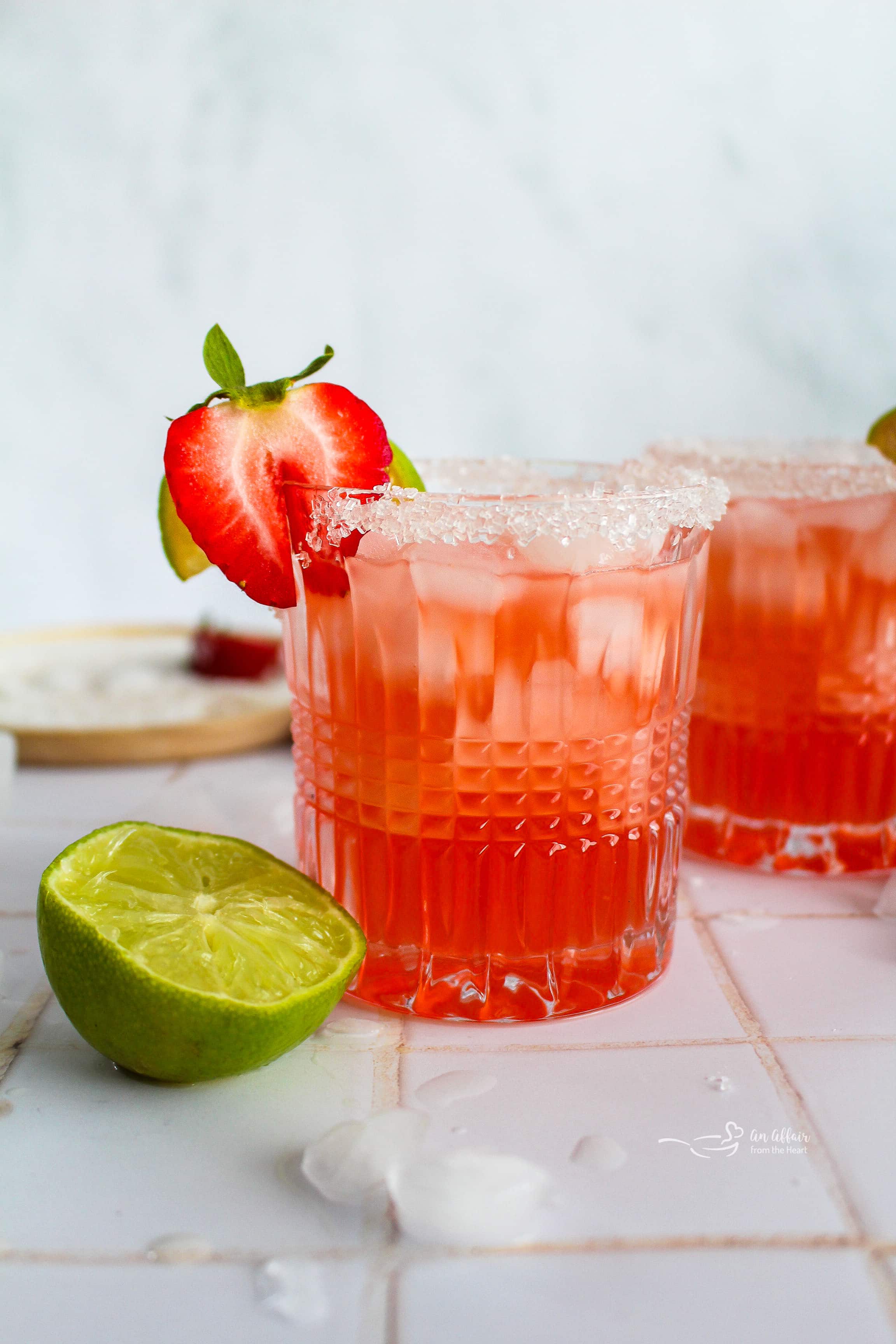 Strawberry Margaritas, one garnished with half a strawberry and a slice of lime.